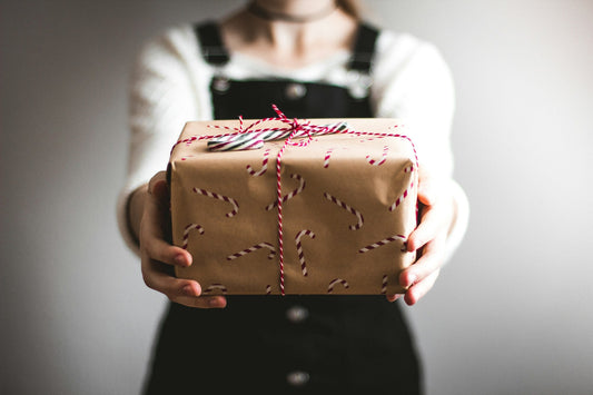 Hands holding out a Christmas gift wrapped in brown paper with a candy cane pattern and red and white twine